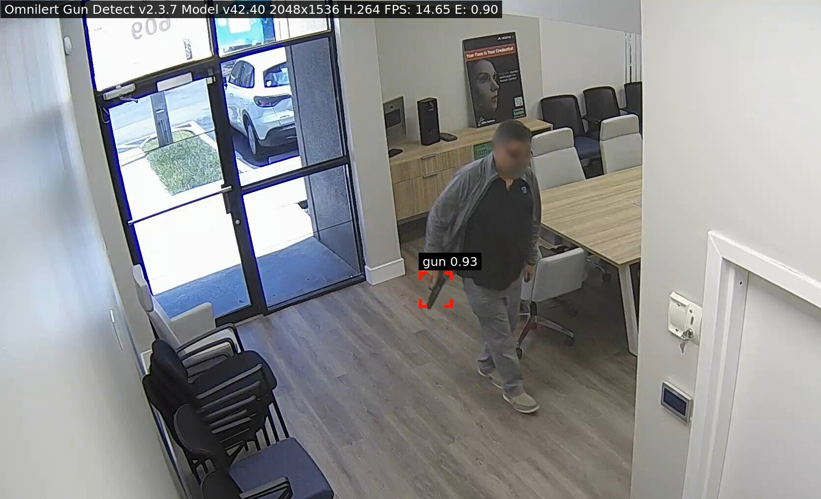 A surveillance camera captures a man walking alone in a white-walled hallway with a blue floor, while a yellow detection box highlights him as part of a security monitoring system.